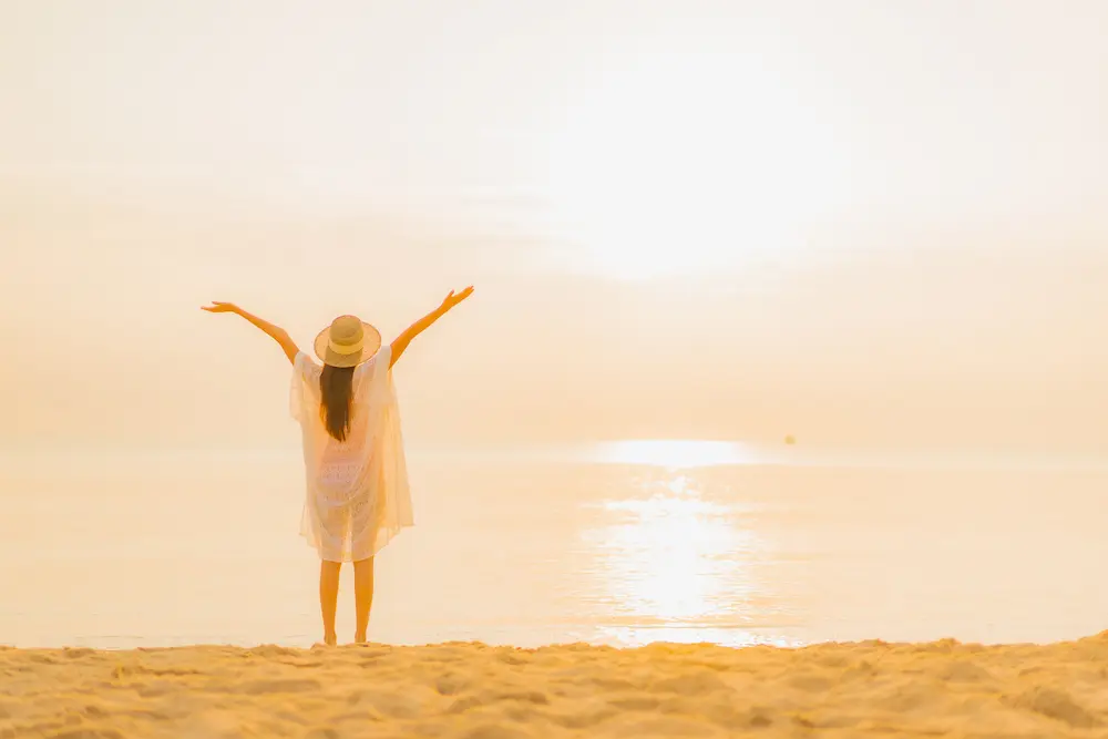 日没のビーチで手を上げている女性